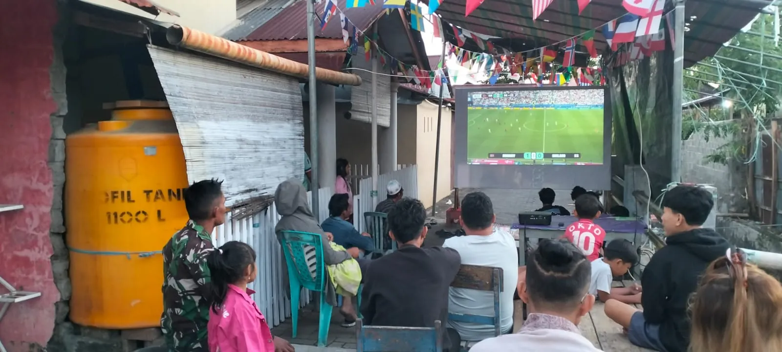 “Babinsa dan Warga Bersatu Dalam Suasana Kebersamaan Nobar Piala Dunia 2026”.